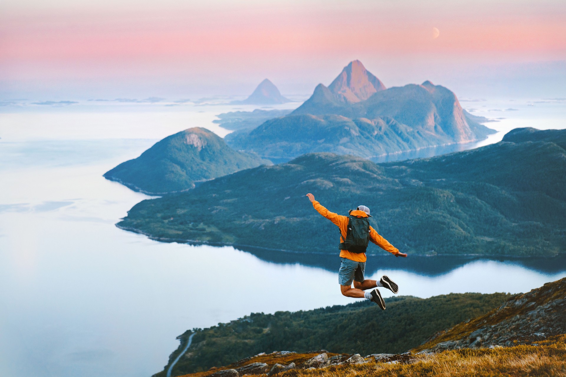 Man traveler jumping in mountains travel in Norway active summer vacations, male tourist hiking solo healthy lifestyle freedom success concept enjoying sunset islands and sea Helgeland landscape
